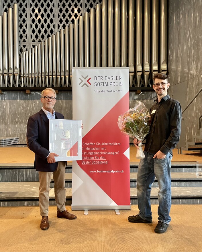 Andreas Cavegn und Fabian Karlen vom Restaurant zum Tell posieren für ein Bild in der Johanneskirche und präsentieren ihre Auszeichnung. Im Hintergrund ist die grosse Kirchenorgel.